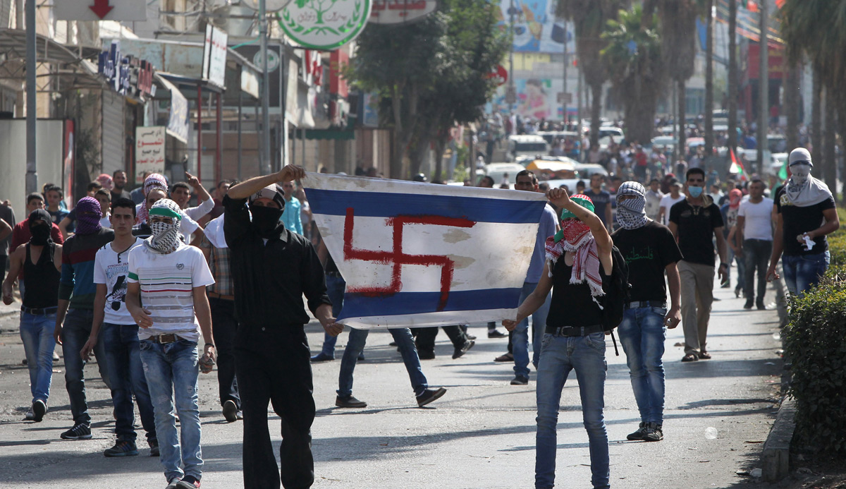 
Palestinian protesters hold up a makeshift Israeli flag, with a swastika replacing the Star of David, during a demonstration in the West Bank city of Hebron on October 16, 2015. HAZEM BADER/AFP/Getty Images.




