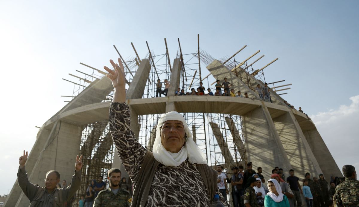 A Syrian Kurdish woman flashes a victory sign during the June 24, 2016 funeral of fighters who died in an attack against Islamic State forces. In the background, a martyrs memorial is under construction. DELIL SOULEIMAN/AFP/Getty Images.
