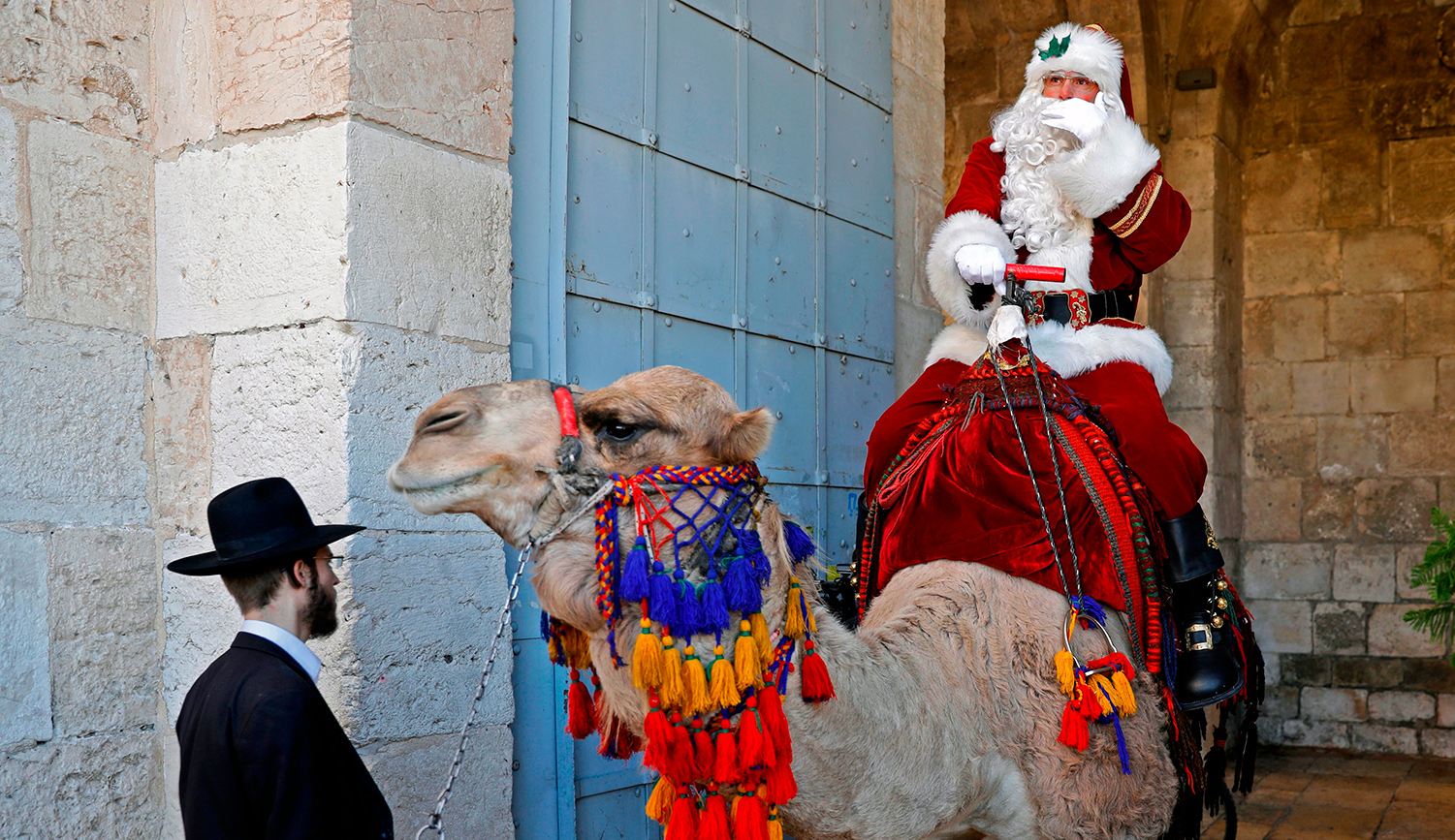 A man dressed up as Santa Claus gestures as he rides a camel before an ultra-Orthodox Jewish man in Jerusalem&#8217;s Old City on December 19, 2019.  AHMAD GHARABLI/AFP via Getty Images.

