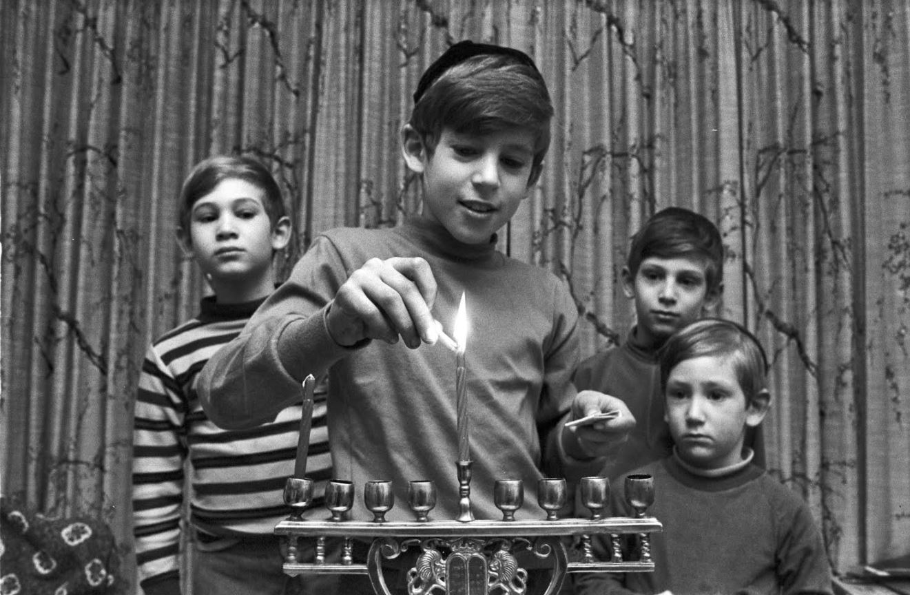 A young Jewish boy lights a menorah for Hanukkah as his brothers look on in Brookline, MA in 1971. Photo by Spencer Grant/Getty Images
