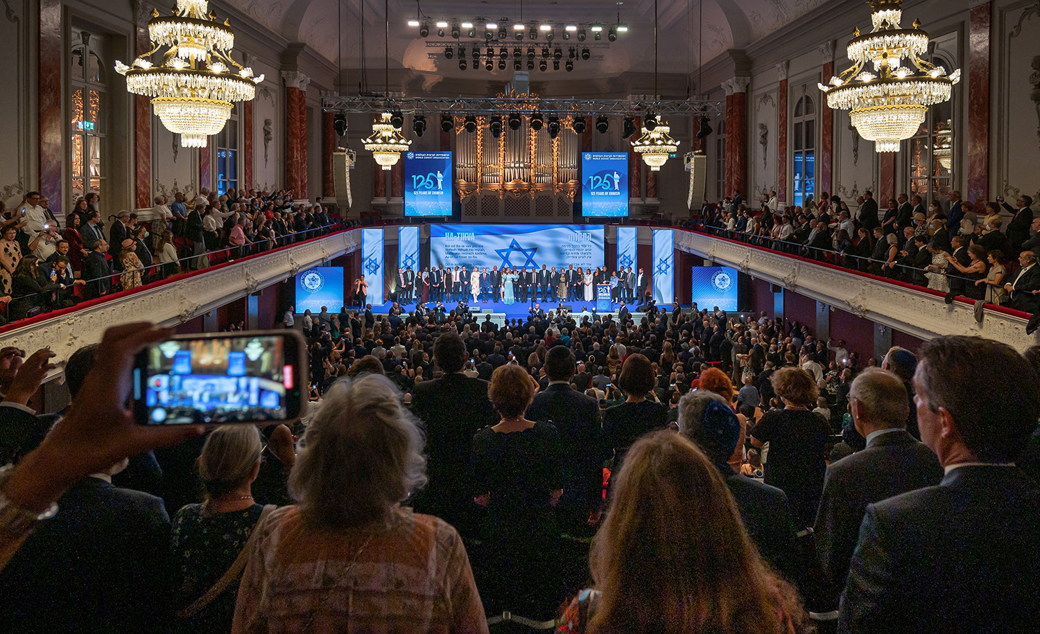 
Guests sing the Israeli national anthem at the end of a gala to mark the 125th anniversary of the First Zionist Congress at Basel&#8217;s historic Stadtcasino on August 29, 2022. FABRICE COFFRINI/AFP via Getty Images.






